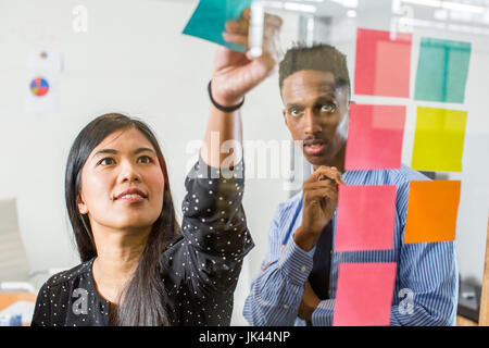 Woman and man reading adhesive notes in office Stock Photo