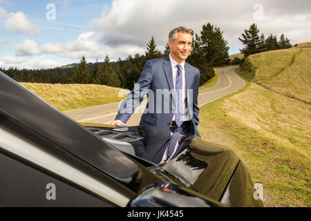 Smiling Caucasian businessman leaning on car Stock Photo