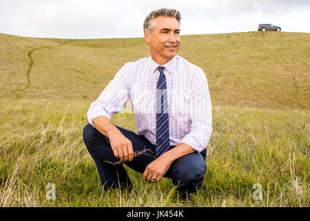 Smiling Caucasian businessman crouching in grass Stock Photo