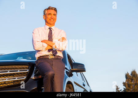 Smiling Caucasian businessman leaning on car Stock Photo