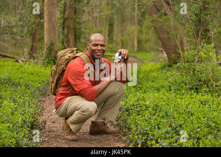 African American man crouching on path in forest holding camera Stock Photo