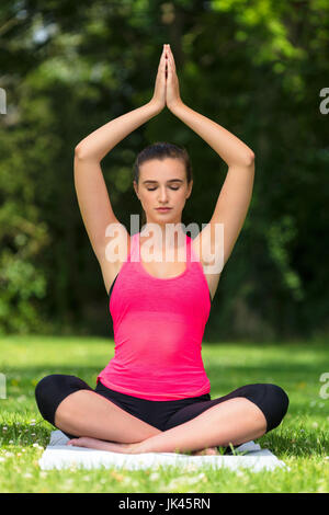 Young fit healthy woman female or girl practicing yoga pose on a mat outside in a natural tranquil green environment Stock Photo