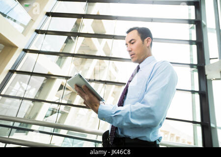 Serious Mixed Race businessmen using digital tablet in lobby Stock Photo
