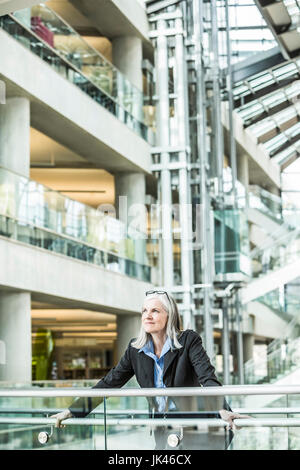 Portrait of pensive Caucasian businesswoman leaning on railing in lobby Stock Photo