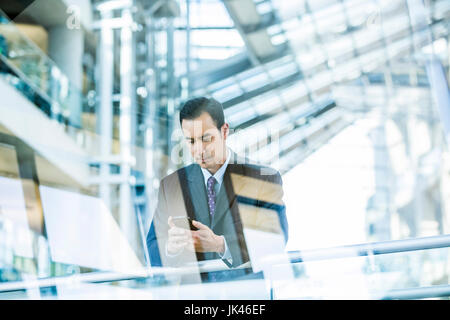 Mixed Race businessman texting on cell phone leaning on railing in lobby Stock Photo