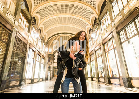 Caucasian man carrying woman piggyback in lobby Stock Photo