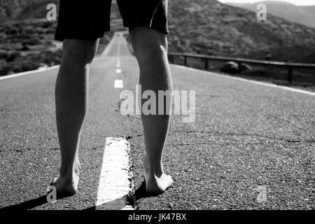 Legs of barefoot Caucasian man standing in middle of road Stock Photo