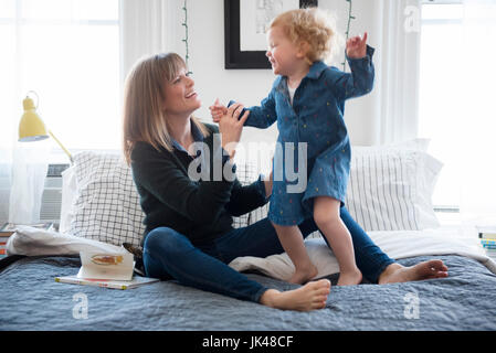 Caucasian mother sitting on bed playing with daughter Stock Photo