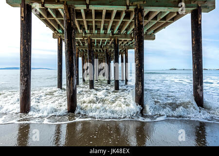 Waves splashing on pilings of wooden pier at beach Stock Photo