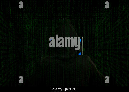 A hacker’s back view, cloaked in shadows, works at a laptop surrounded by a green code matrix, mysterious and high-tech nature of cyber activities Stock Photo