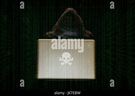 A hacker, shrouded in anonymity, works on a laptop surrounded by cascading code, with a sinister skull as logo on laptop, cyber threats concept Stock Photo