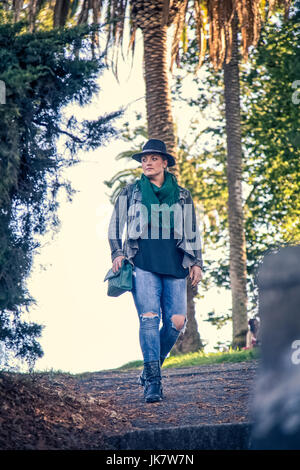 A fashionable, 30-something woman walks through a city park filled with trees. Stock Photo