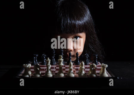 Asian Little Chinese girl playing chess in isolated black background Stock Photo