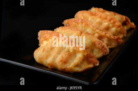 Deep fried gyoza crispy and golden colour set on black plate with studio lighting. Stock Photo