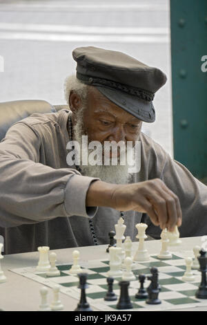 A chess player with a white beard moving a piece during a match at Union Square Park in lower Manhattan, New York City. Stock Photo