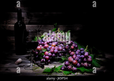 Fresh red grapes bunch lying on leaves on an old wooden table. Photographed with light painting technique Stock Photo