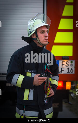 German fire fighter at fire truck observing column of fire at solstice celebrations and midsummer festival Stock Photo