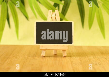 Small empty slate in width to write a message that is posed on an easel all on wooden floor and green foliage background Stock Photo
