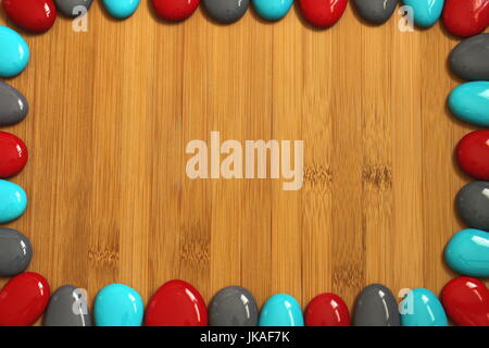 Small red gray and blue pebbles arranged all around a brown bamboo wood floor with an empty space to write a message Stock Photo