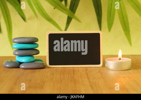 Small empty slate in width to write a message posed on the bamboo floor with gray and blue stones columns in the lifestyle Zen with a candle all on wo Stock Photo