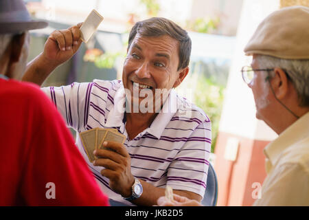 Happy active retired people, old hispanic friends having fun, seniors playing cards at home. Stock Photo