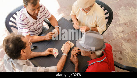 Happy active retired people, old hispanic friends having fun, seniors playing cards at home. Stock Photo