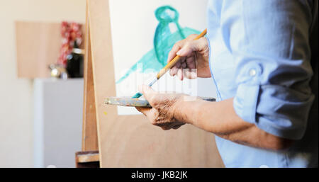 Elderly woman painting for hobby. Active senior person at art school. Closeup of old female hand with brush and palette, mixing color paints Stock Photo