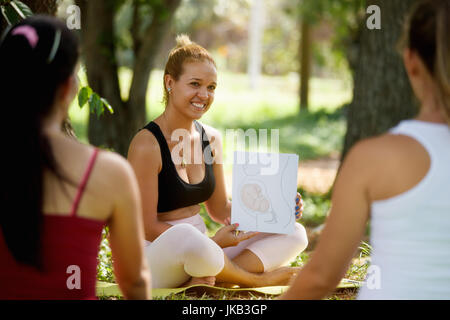 Pregnant women taking prenatal lesson in park. Teacher explaining baby growth inside belly with pictures and drawings. Stock Photo