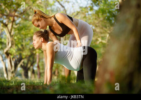 Mom with back pain, mother during pregnancy. Prenatal lesson in city park, antenatal class outdoor. Yoga teacher, midwife, personal trainer, counselor Stock Photo