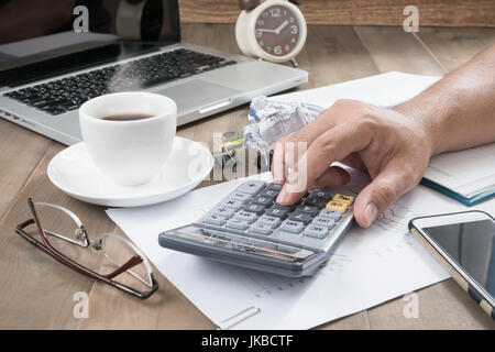 business man using calculator with hot coffee and computer notebook on wood table, business work concept Stock Photo