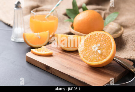 Fresh sliced orange on wood plate and orange juice with sack and black stone background. Stock Photo