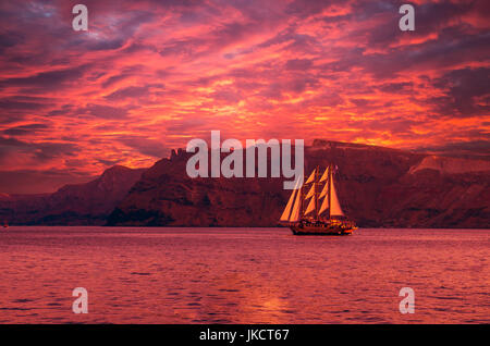 Sailboat in Santorini, Greece. Sailing ship navigate near an island in Cyclades. The photo is taken at sunset. Stock Photo