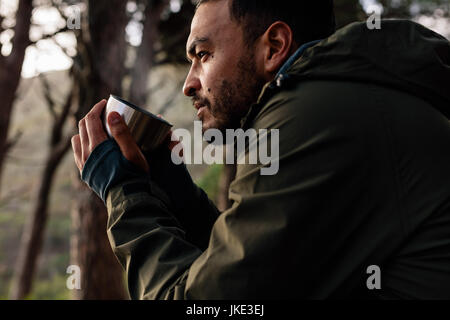 Close up shot of young man drinking hot coffee, taking break during hiking. Male hiker taking rest outdoors. Stock Photo
