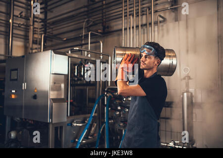 Shot of young man with metal beer barrels at brewery. Brewer carrying keg at brewery plant. Stock Photo