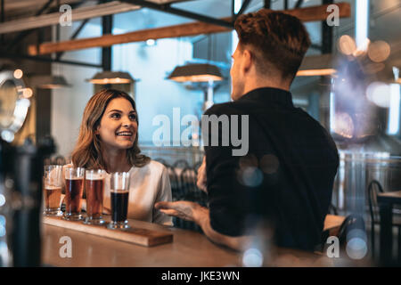 Young couple at bar with different craft beers on a wooden table. Man and woman talking at the bar counter. Stock Photo