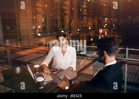 Businesswoman sitting at cafe table with man discussing business. Business people waiting at airport lounge with laptop. Stock Photo