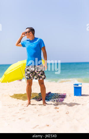 A man carrying a green umbrella and standing on the beach looking on the beach. Summer time Stock Photo