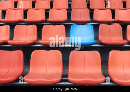 A blue chair amidst rows of orange plastic spectator seats, competition concept Stock Photo