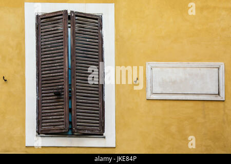 White marble classic blank nameplate with empty space for text and numbers with wooden window on yellow painted wall of old Italian house in Rome. Vin Stock Photo