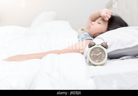 alarm clock on bed with sick child lying down suffering from a headache Stock Photo