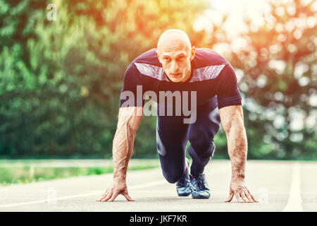 Bald Athletic Man in Running Start Position and Looking Into the Distance in stadium. Stock Photo