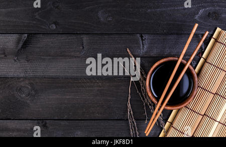 Bamboo mat, soy sauce, chopsticks on dark table Stock Photo