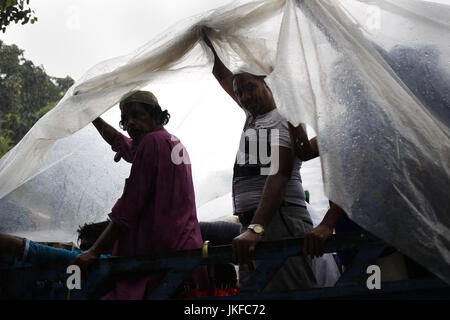 Dhaka, Bangladesh. 23rd July, 2017. Bangladeshi commuters save themselves by a plastic paper sheet from heavy rain on the street, Dhaka. A monsoon shower hit the city and disrupted daily life. The Bangladeshi monsoon season usually takes place between June and July. Credit: Md. Mehedi Hasan/ZUMA Wire/Alamy Live News Stock Photo