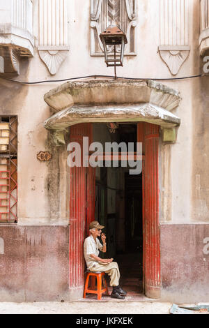 Havana street scene, Cuban man smokng a cigar in front of an art deco building entrance, Cuba Stock Photo