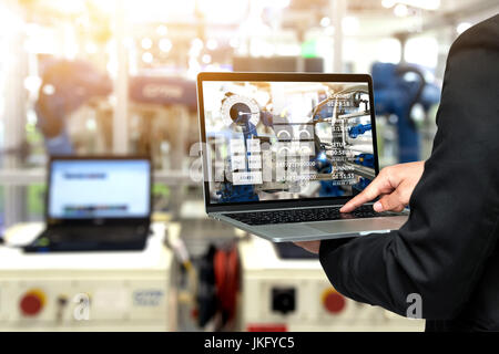 Engineer hand using laptop with machine real time monitoring system software. Blur automation robot arm machine in smart factory Industry 4th iot , di Stock Photo