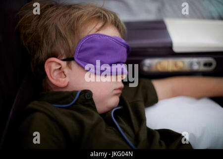 New York City,  United States,  JFK Airport a small child boy sleep on a long haul flight using the mask to cover his eyes Stock Photo