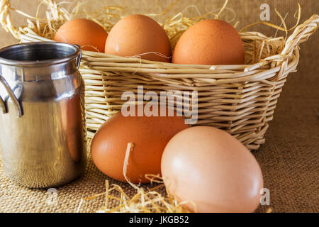 Three Eggs in a Basket and two eggs placed on the foreground with a Mini Milk Urn on the left hand side on a Hessian Background. Stock Photo