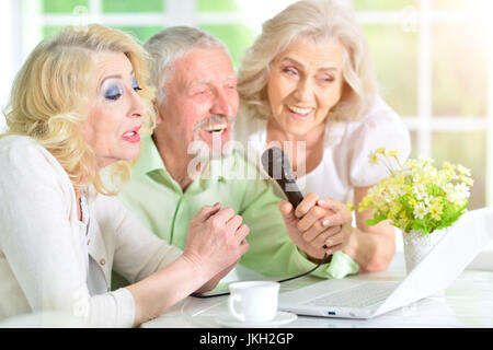 group of senior people sitting at table using laptop and singing karaoke Stock Photo
