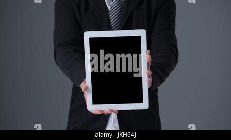 Businessman holding tablet in black suit on gray background Stock Photo