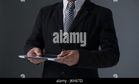Businessman holding tablet in black suit on gray background Stock Photo